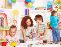 Children with teacher painting at easel in school.